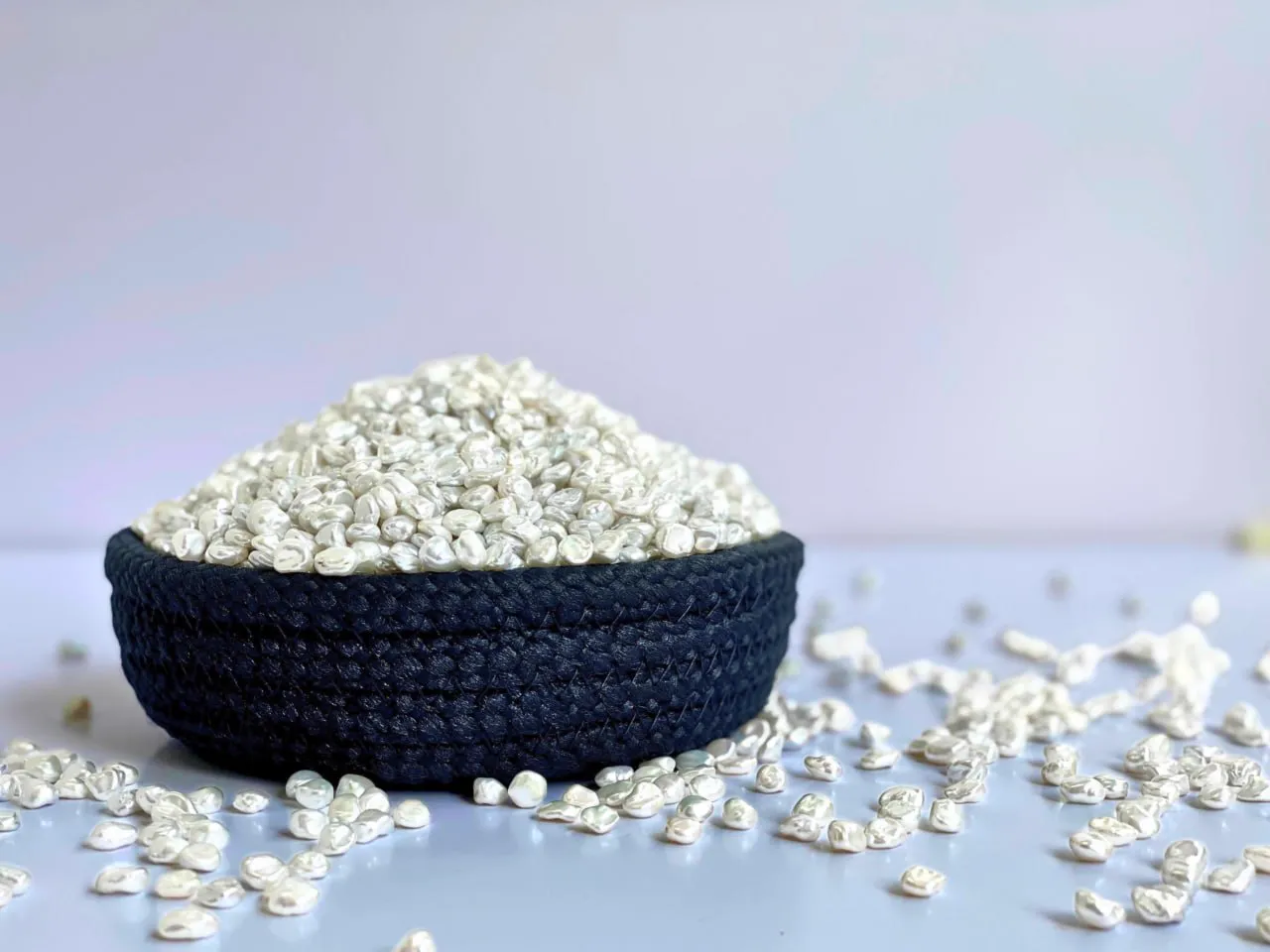 Loose white freshwater pearls heaped in a dark woven bowl